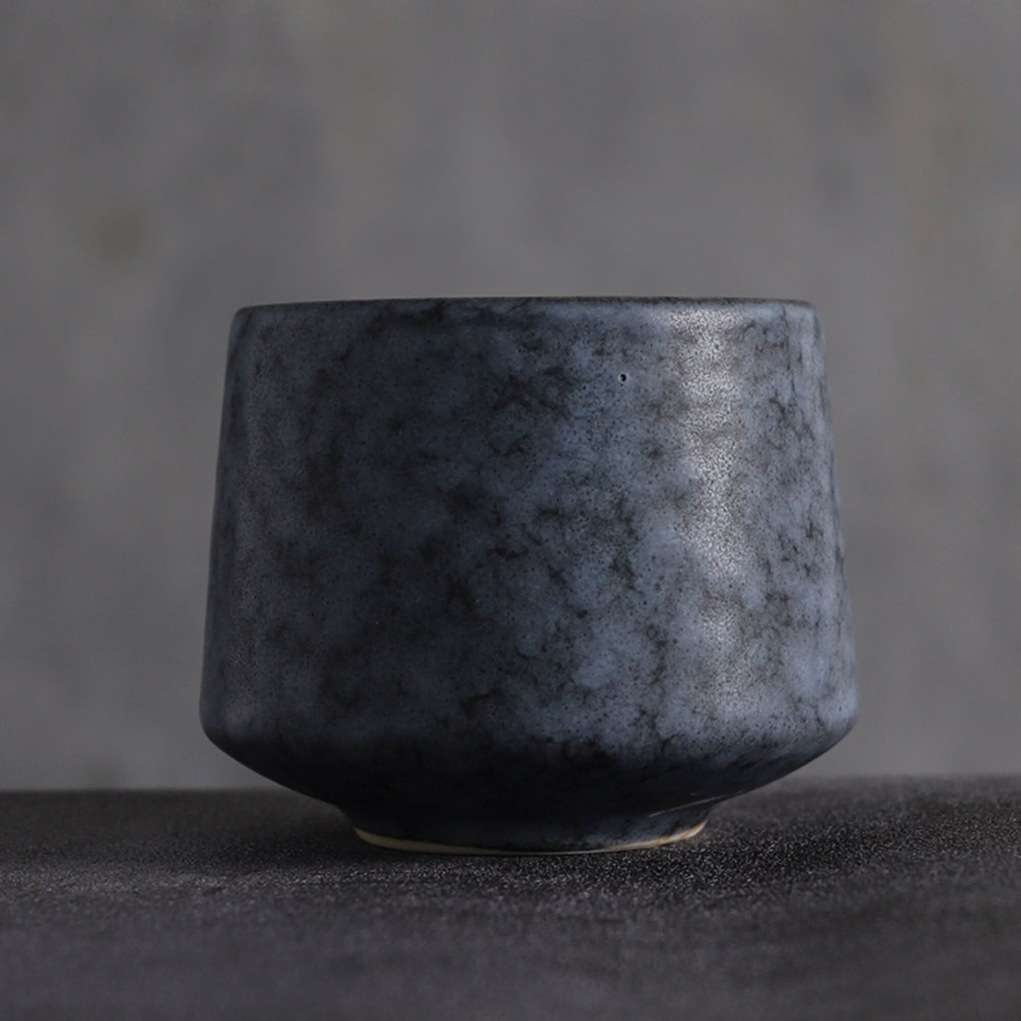 Japanese tea cup with gray tones and speckled texture, on dark textured surface.
